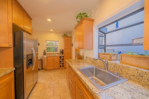 A kitchen with wooden cabinets, a stainless steel refrigerator, granite countertops, and a large window with a view.