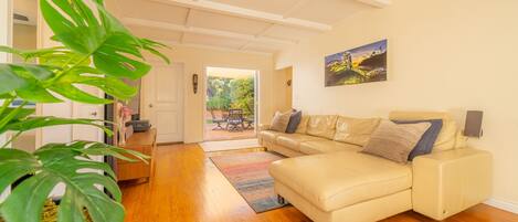 A living room with a beige sofa, a potted plant, and a wooden floor.
