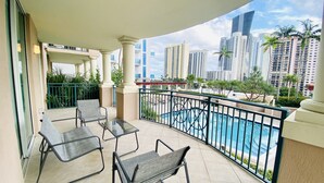 Un balcon avec trois fauteuils de jardin, une piscine et une vue sur les immeubles de grande hauteur.