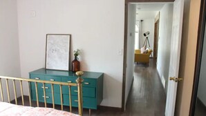 A bedroom with a bed, a teal dresser, a framed picture, and a small vase.