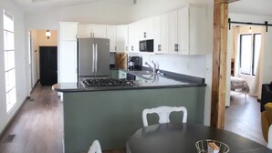 A modern kitchen with white cabinets, a central island, stainless steel appliances, and a dining area with a table and chairs.