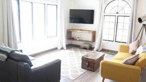 A living room with a black sofa, a yellow armchair, a wooden coffee table, and a TV on the wall.
