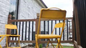 A wooden deck with two yellow chairs and a brick building in the background.