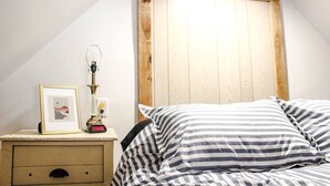 Un dormitorio con cabecera de madera, mesita de noche con lámpara, cuadro enmarco y ropa de cama a rayas.