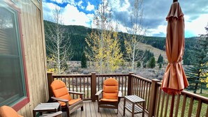 A wooden deck with outdoor seating, including chairs and tables, overlooking a forested hillside. - Private Garage/Walk to the Gondola in 2 Minutes/Pool and Hot Tub/Fitness Room (Keystone)