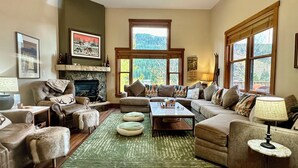 A cozy living room with a fireplace, comfortable seating, and large windows offering a view of the outdoors. - Private Garage/Walk to the Gondola in 2 Minutes/Pool and Hot Tub/Fitness Room (Keystone)