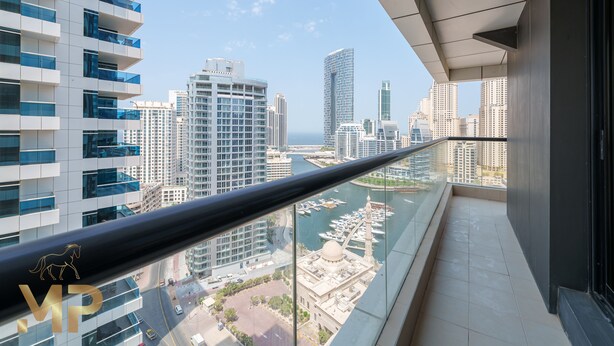 Un immeuble de grande hauteur doté d’un balcon en verre offrant une vue sur un port de plaisance et le paysage urbain.
