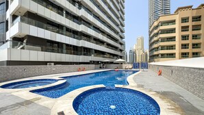 Un bâtiment moderne doté d’une piscine sur le toit, ornée de mosaïques bleues et d’une terrasse carrelée en pierre.