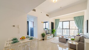 Un salon moderne comprenant un canapé, une table à manger avec des chaises, un téléviseur et une grande fenêtre avec des rideaux.