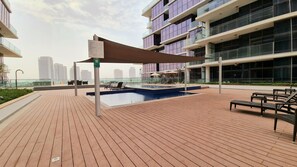 Un espace piscine aménagé sur le toit, avec une terrasse en bois, des chaises longues et un auvent ombragé.