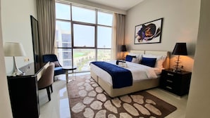 Ein Hotelzimmer mit einem großen Bett, einem Schreibtisch, einem Sessel und Blick auf die Stadt durch große Fenster.