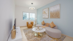 A modern living room with a sofa, a coffee table, a TV, and artwork on the wall. - Marco Polo - 1BR with Marina Views, Near Metro & Marina Mall (Dubai)