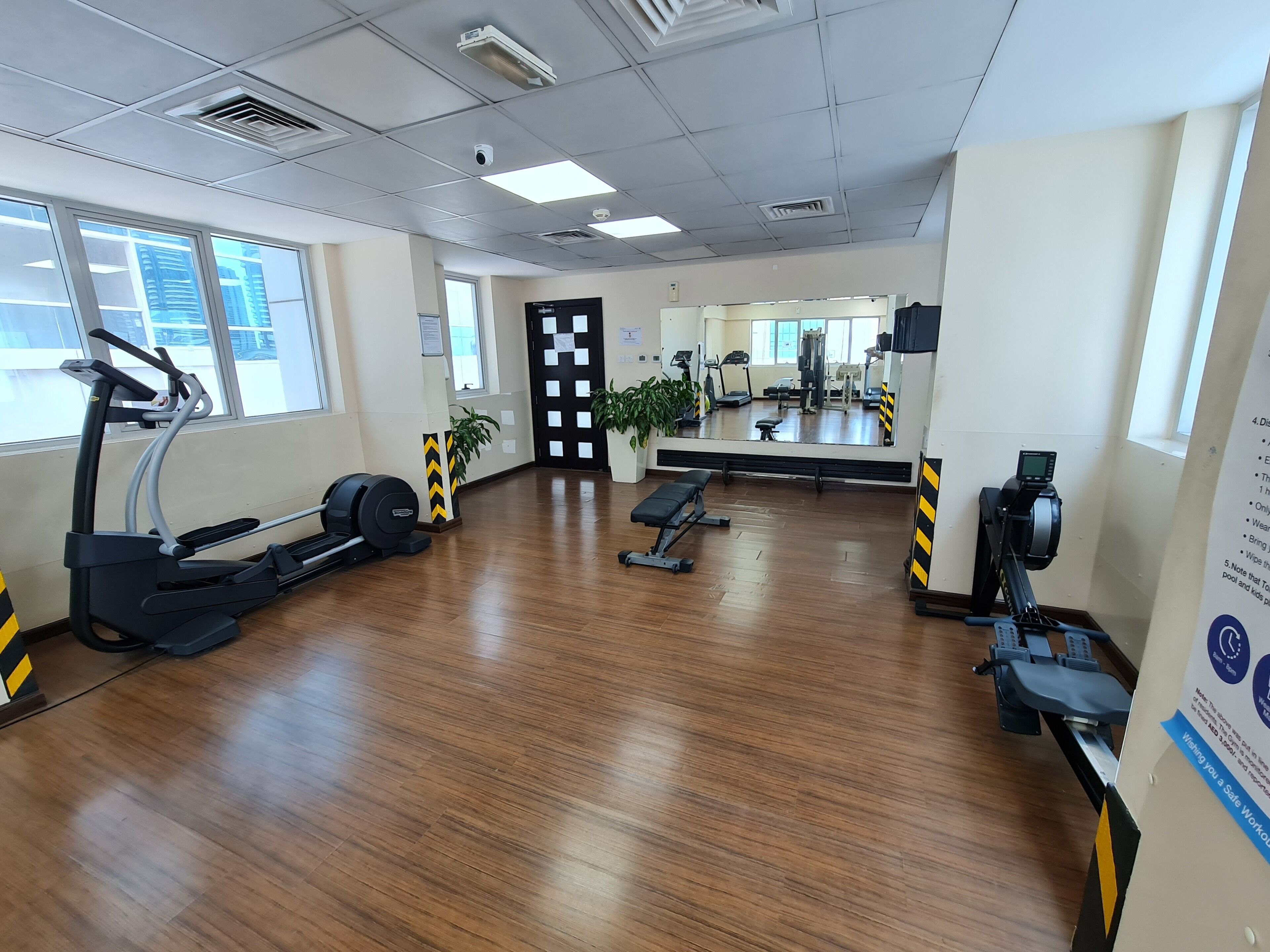A gym with exercise equipment, wooden flooring, and large windows.