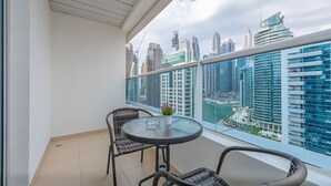A balcony with a glass table and wicker chairs, overlooking a cityscape with modern buildings and a marina. - Marco Polo - 1BR with Marina Views, Near Metro & Marina Mall (Dubai)