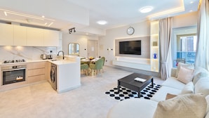 A modern apartment with a kitchen, dining area, and living room. It includes a flat-screen TV, a sofa, and a coffee table. - Marco Polo - 1BR with Marina Views, Near Metro & Marina Mall (Dubai)