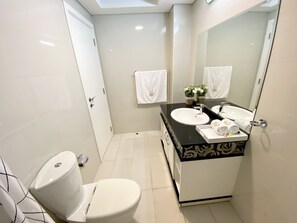 A modern bathroom with a white toilet, a black vanity with a white sink, and a large mirror. There are two white towels hanging on the wall and a small potted plant on the vanity. -  Luxe Apt with Panoramic Views and Terrace (Dubai)