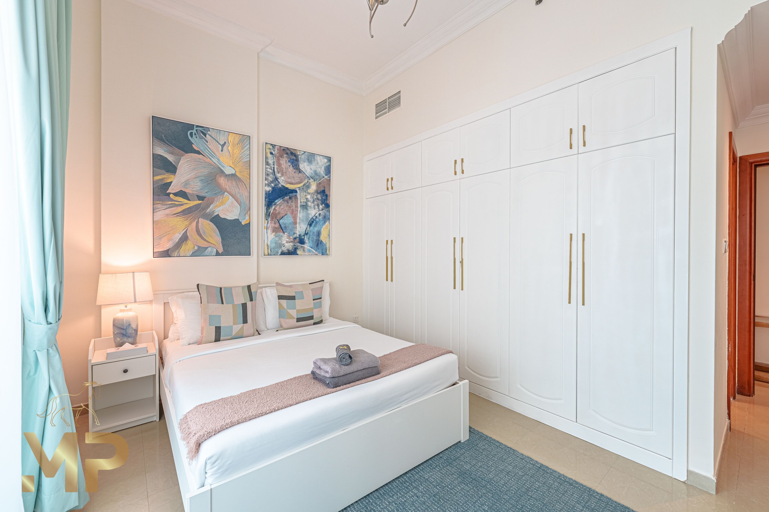 A bedroom with a bed, nightstands, a wardrobe, and abstract wall art.