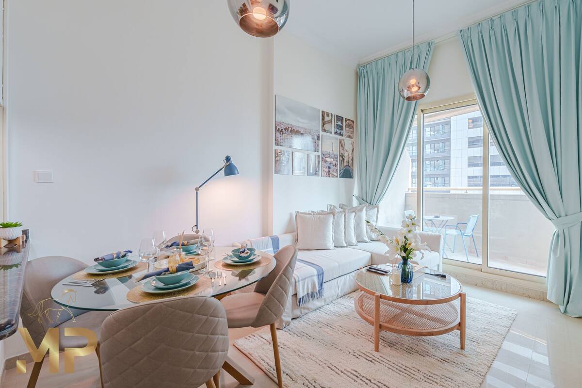 A modern living room with a dining table set for four, a sofa, a coffee table, and a large window with curtains.