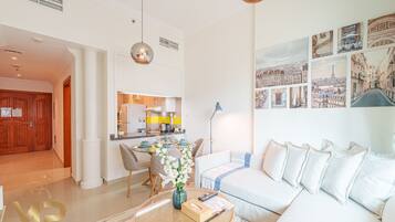 A modern living room with a sofa, a coffee table with a vase, and a dining area with chairs and a kitchen in the background.