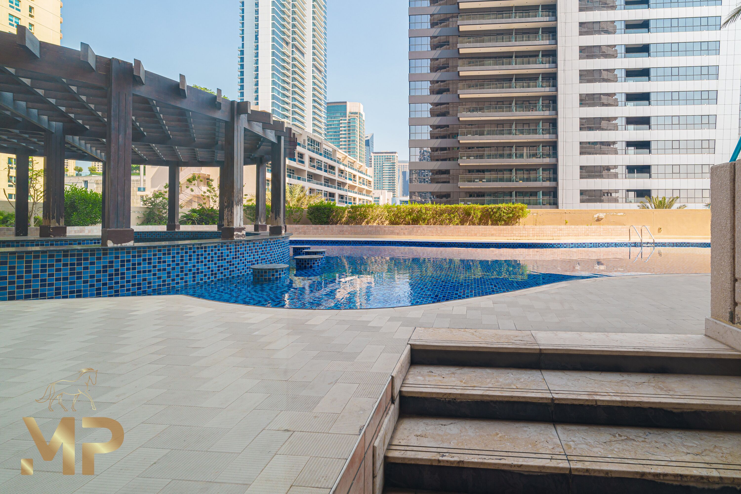 A swimming pool area with a pergola structure, steps leading to the pool, and modern high-rise buildings in the background.
