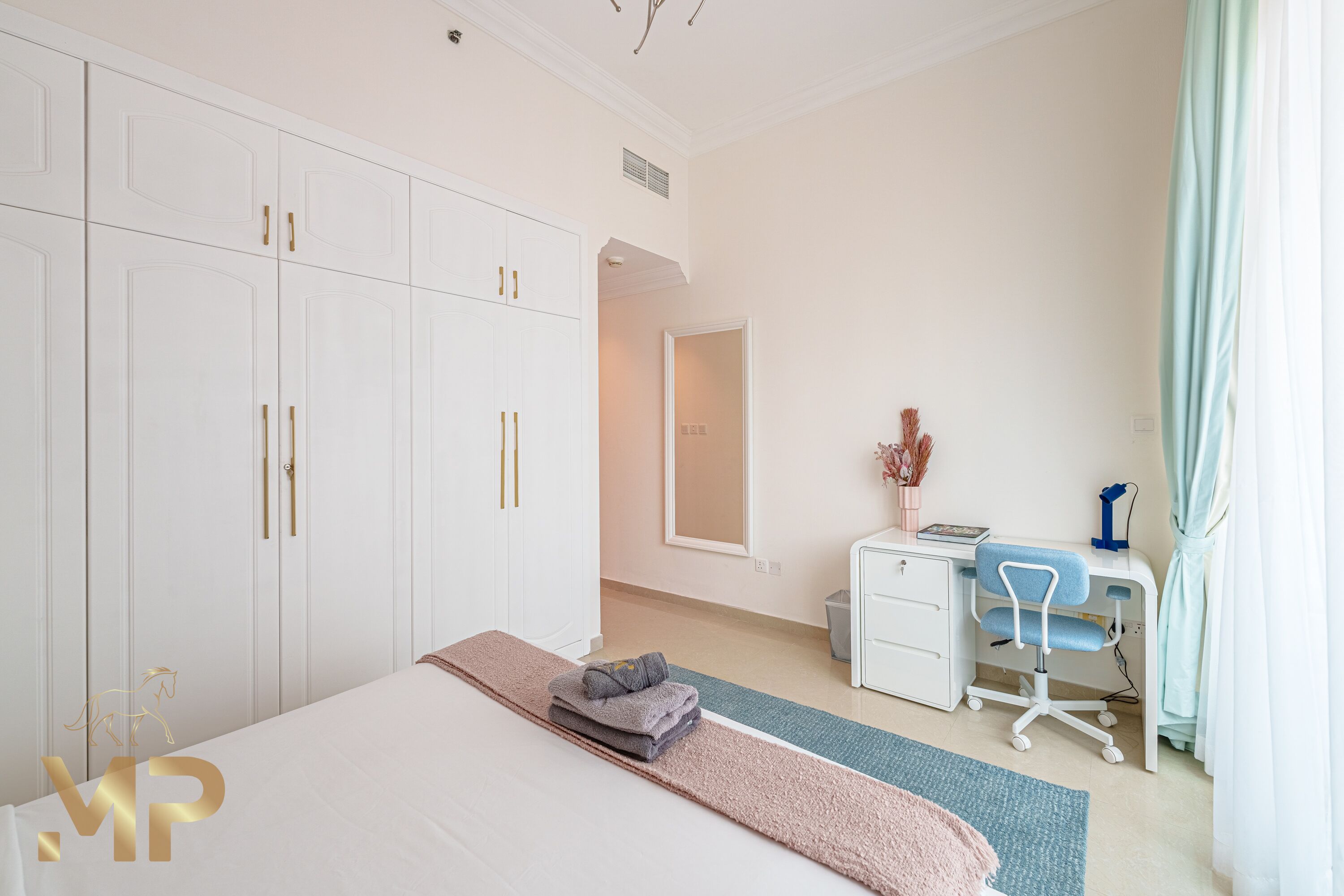 A hotel room with a large bed, a desk with a chair, a wardrobe, and a mirror.