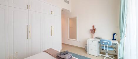 A hotel room with a large bed, a desk with a chair, a wardrobe, and a mirror.