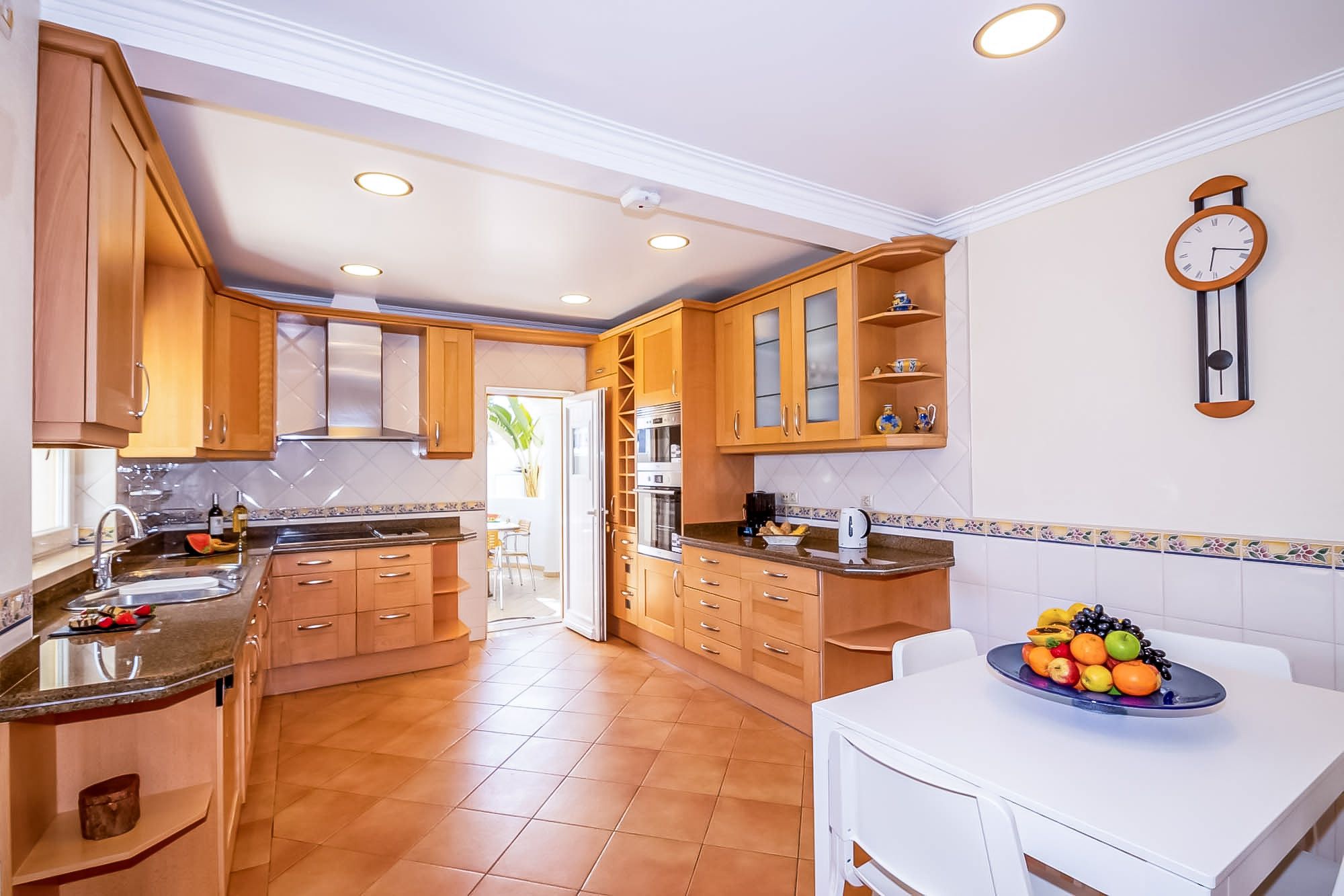 A kitchen with wooden cabinets, a white countertop, and a fruit bowl on the table.