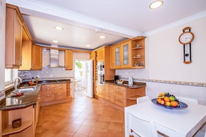 A kitchen with wooden cabinets, a white countertop, and a fruit bowl on the table.