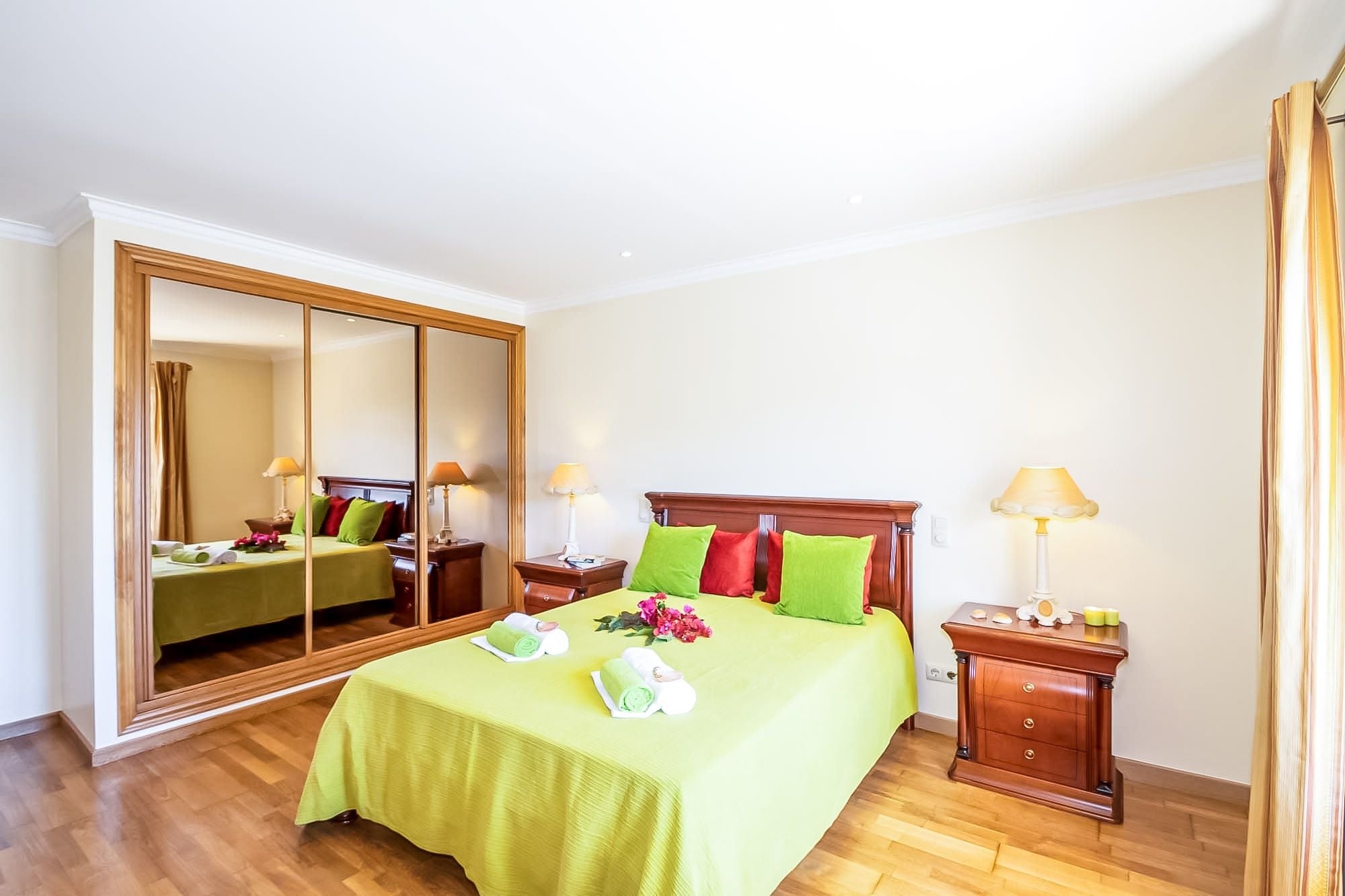 Une chambre d’hôtel avec un grand miroir, un lit avec une literie verte, une table de chevet avec une lampe et un plancher en bois.