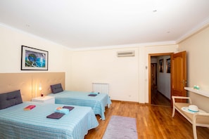 A bedroom with two beds, a radiator, a nightstand, a bedside lamp, a framed picture on the wall, and a wooden chair.