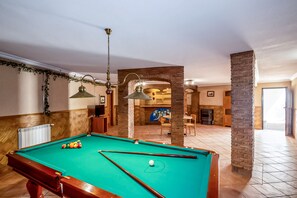 A pool table in a room with a fireplace, wooden walls, and a hanging light fixture.