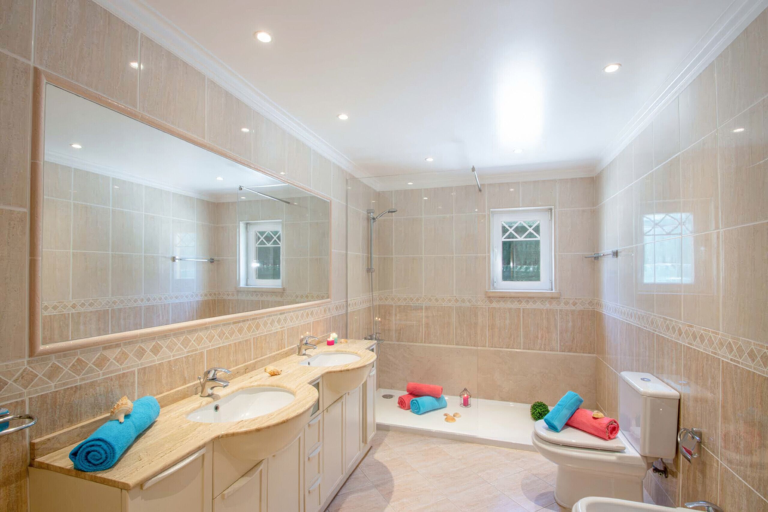A bathroom with a large mirror, two sinks, a bathtub, and a toilet.