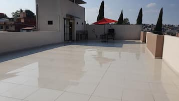 A rooftop terrace with a tiled floor, a barbecue grill, and a red umbrella.