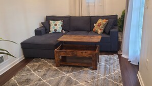 A living room with a dark grey sofa, a wooden coffee table, and a patterned rug. - Entire Lovely Apt* 5 Miles to EWR* Free Parking (Linden)