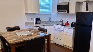 A modern kitchen with white cabinets, a black refrigerator, and a dining table with chairs. - Entire Lovely Apt* 5 Miles to EWR* Free Parking (Linden)