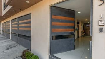 A modern building entrance with a large sliding door, a small garden area, and a clean tiled floor.