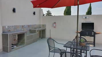 An outdoor patio with a tiled kitchen area, a barbecue grill, and a table with chairs.