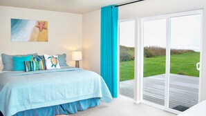 A bedroom with a bed, a window with a view of a grassy area, and a door to an outdoor deck. - Ocean Front, Amazing Views! Hot Tub! Dog Friendly! (Yachats)