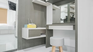 A modern bathroom with a grey and white color scheme, a built-in shelf with toiletries, a mirror, and a small stool. - Comfort Studio at Menteng Square Apartment (Jakarta)