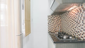 A kitchen with a tiled backsplash, stainless steel appliances, and a window with a curtain. - Comfort Studio at Menteng Square Apartment (Jakarta)