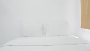 A simple, unadorned bed with white linens and pillows in a minimalistic room. - Comfort Studio at Menteng Square Apartment (Jakarta)