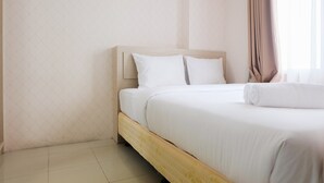 A neatly made bed with white linens and a wooden headboard in a room with light-colored walls and a window with curtains.