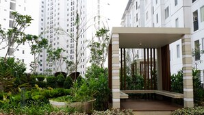 Un bâtiment moderne doté d’une entrée couverte, entouré d’une végétation luxuriante et bordé, au loin, d’immeubles résidentiels imposants.