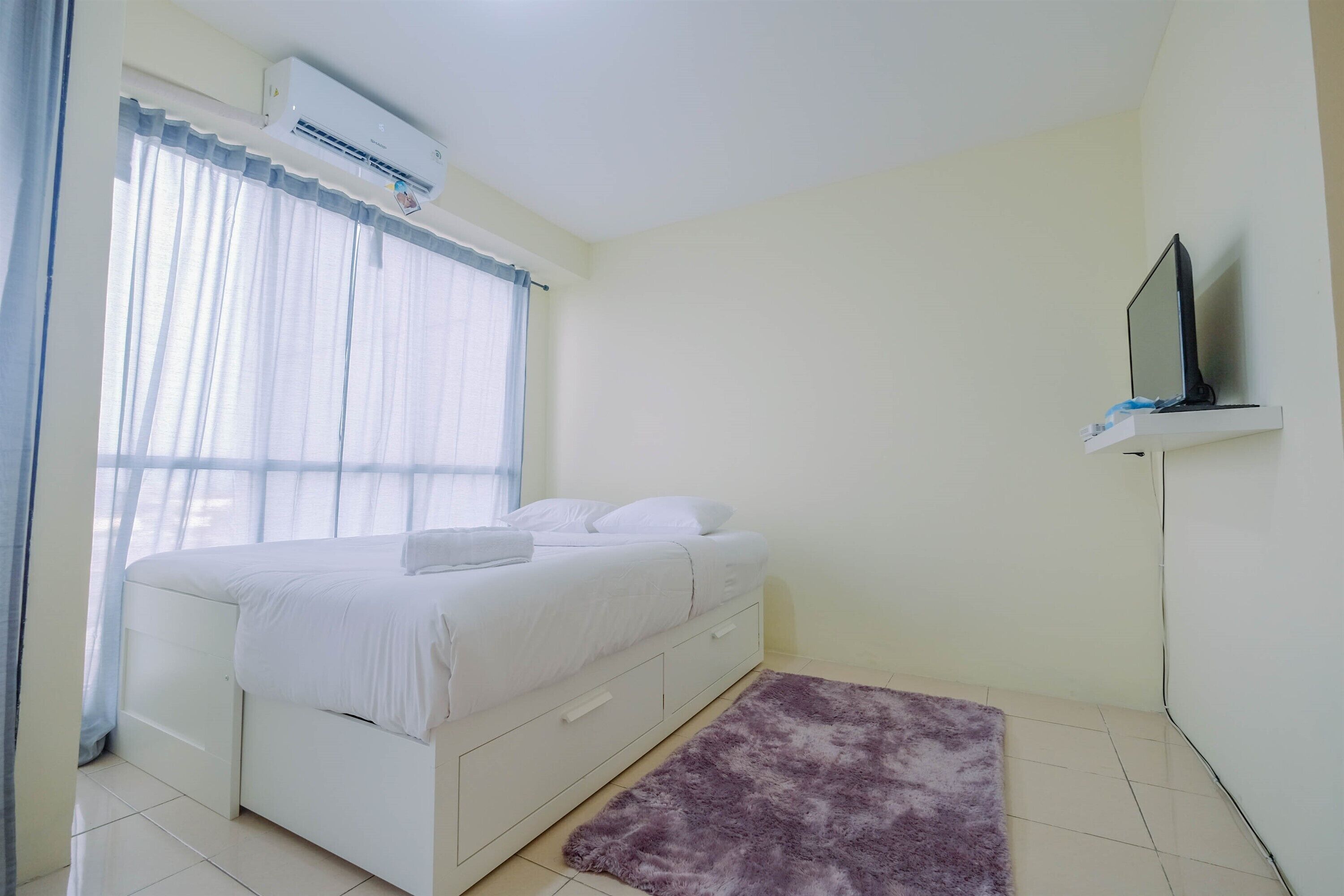 A bedroom with a bed, a TV on a stand, and a window with curtains.