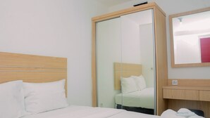 A hotel room with a wooden headboard, a bed with white bedding, a glass wardrobe, and a mirror on the wall.