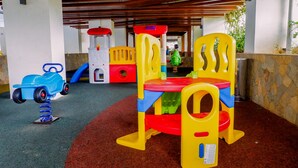 A children's play area with a colorful play structure, a small blue toy car, and a child in the background.