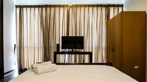 A hotel room with a large bed, a television on a stand, and a wardrobe.
