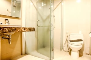 A bathroom with a glass-enclosed shower, a sink with a marble countertop, and a toilet with a towel on it. - Best Location 1BR The Mansion at Kemang Apartment (Jakarta)