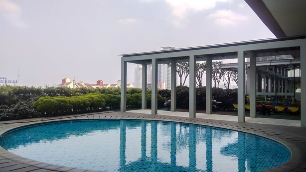 A swimming pool with a tiled edge, surrounded by a covered area with columns, and a view of distant buildings.