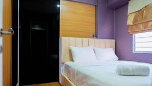Une chambre d’hôtel avec un lit, un plancher en bois, une porte et une fenêtre avec des rideaux.
